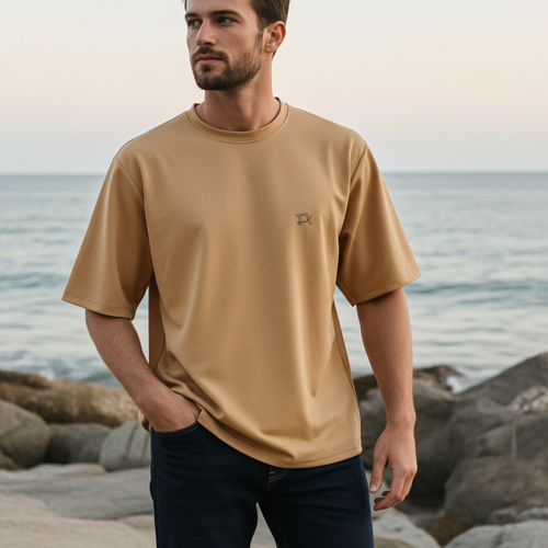 Man wearing a beige t-shirt standing on a beach with ocean in the background