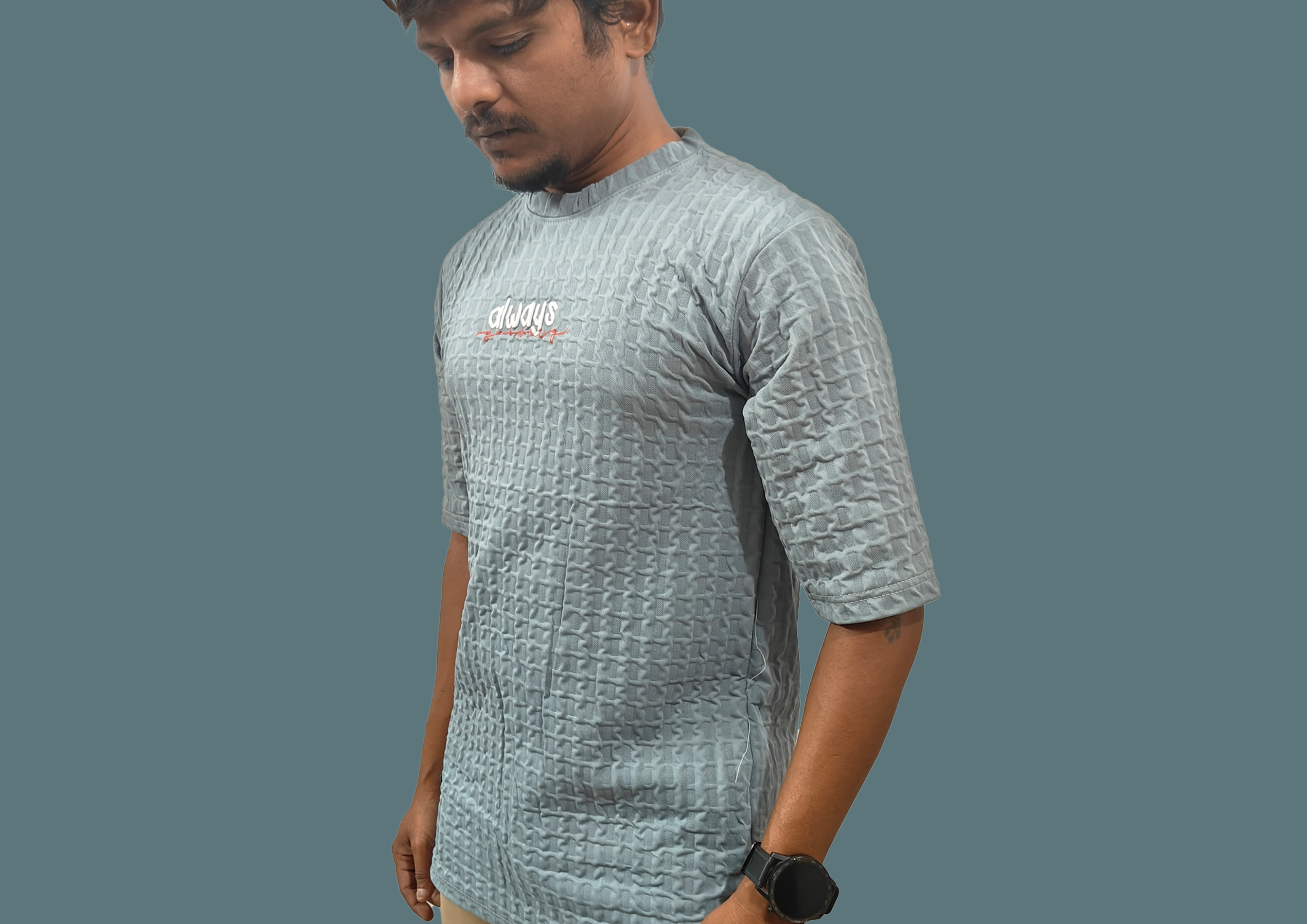 Man wearing a textured gray t-shirt with a logo on a plain background