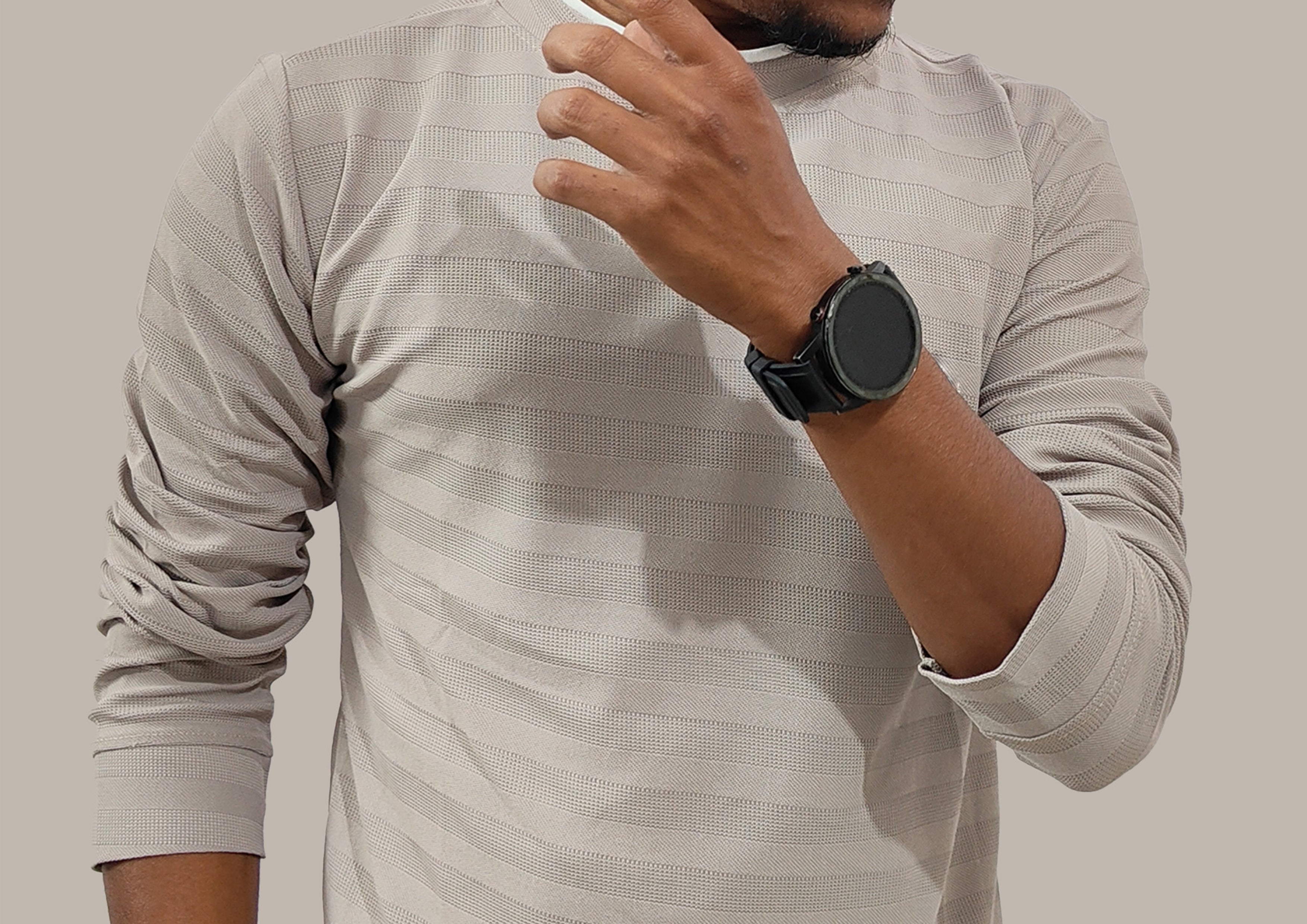 Man wearing a light gray long-sleeve shirt and a smartwatch on a plain background