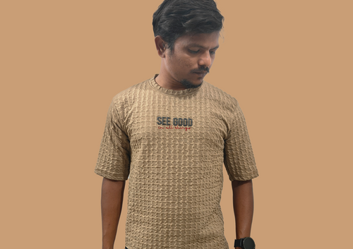 Man wearing a textured beige t-shirt with 'SEE GOOD' text on a brown background