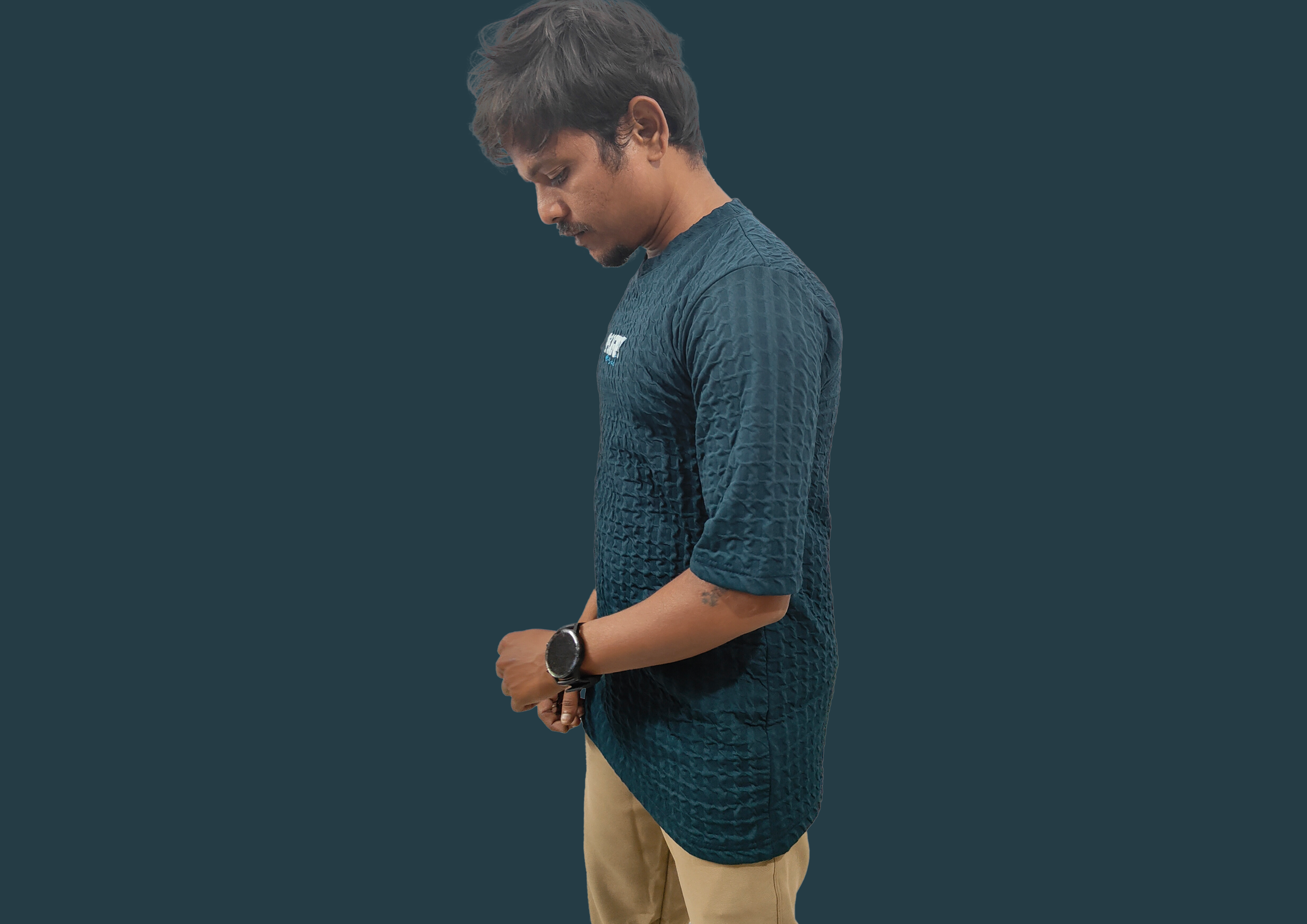 Man wearing a dark green textured shirt and beige pants on a black background