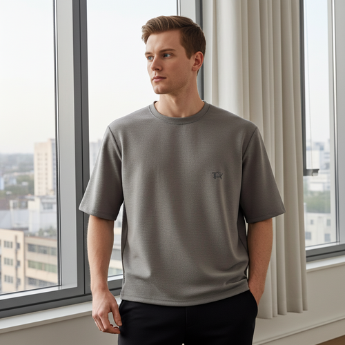 Clean Minimal Look Premium Gay Oversize T-shirt for Men front view oversized streetwear style Man wearing a gray t-shirt standing in front of large windows with a cityscape view.